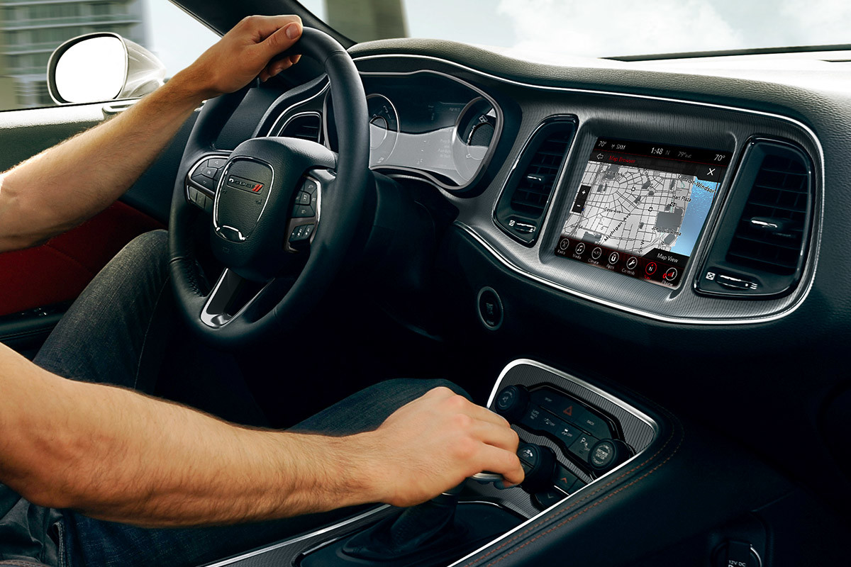 Image of the Uconnect 4C touchscreen displaying Navigation information. Hands are grasping the steering wheel and shifter.