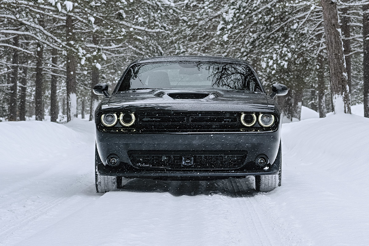 A black 2022 Dodge Challenger being driven on a snowy road through a forest.