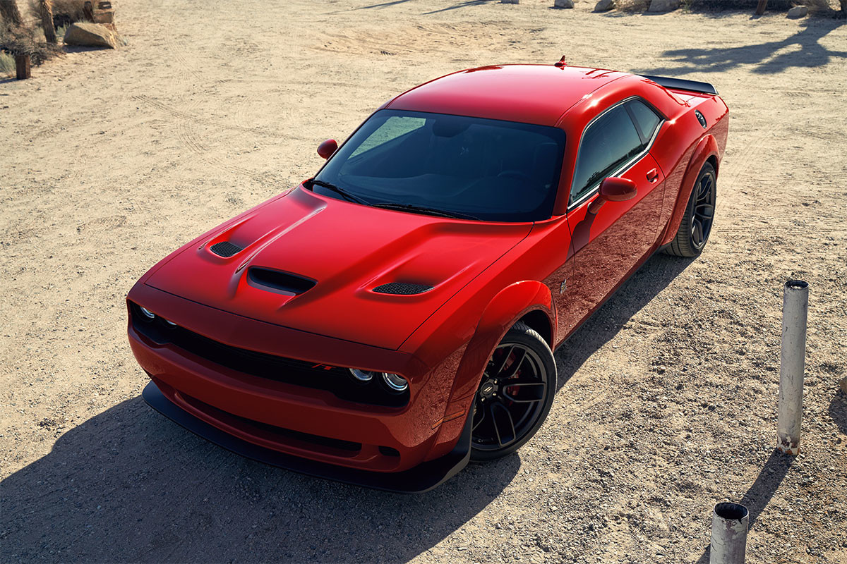 Une Dodge Challenger 2022 rouge roulant sur une route pavée bordée d’arbres.