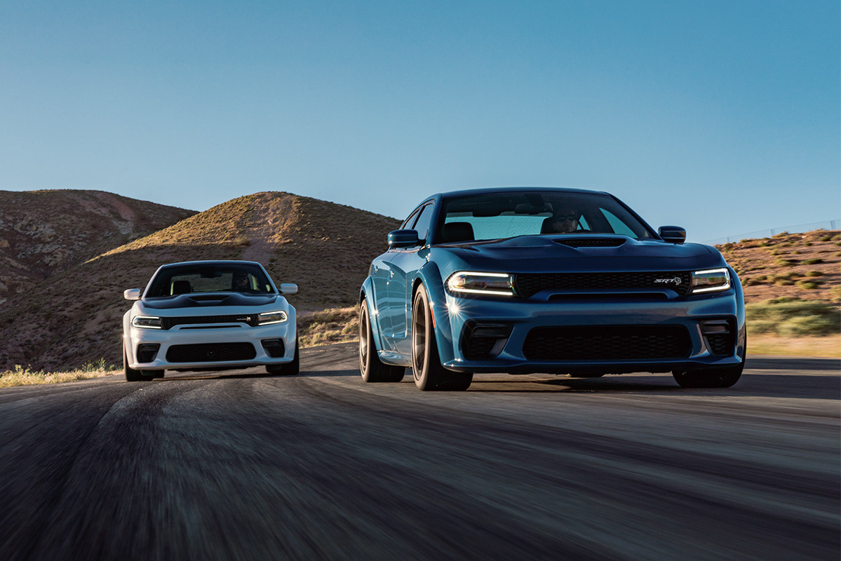 The blue 2020 Dodge Charger driving in front of the white 2020 Dodge Charger on a road in a desert
