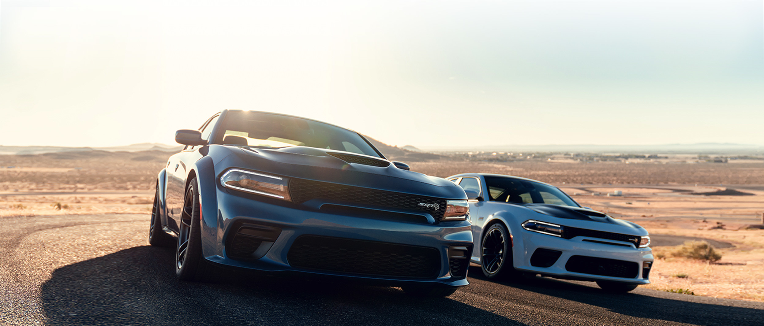 The blue 2020 Dodge Charger being driven on a road in a desert beside the white 2020 Dodge Charger