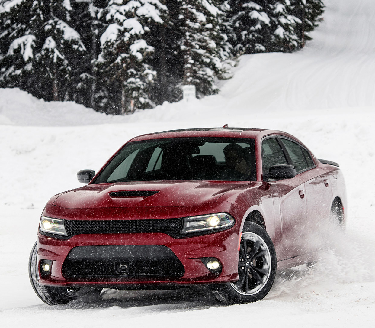 Burgundy Dodge Charger at the bottom of a snowy hill with snow-covered trees in the background.