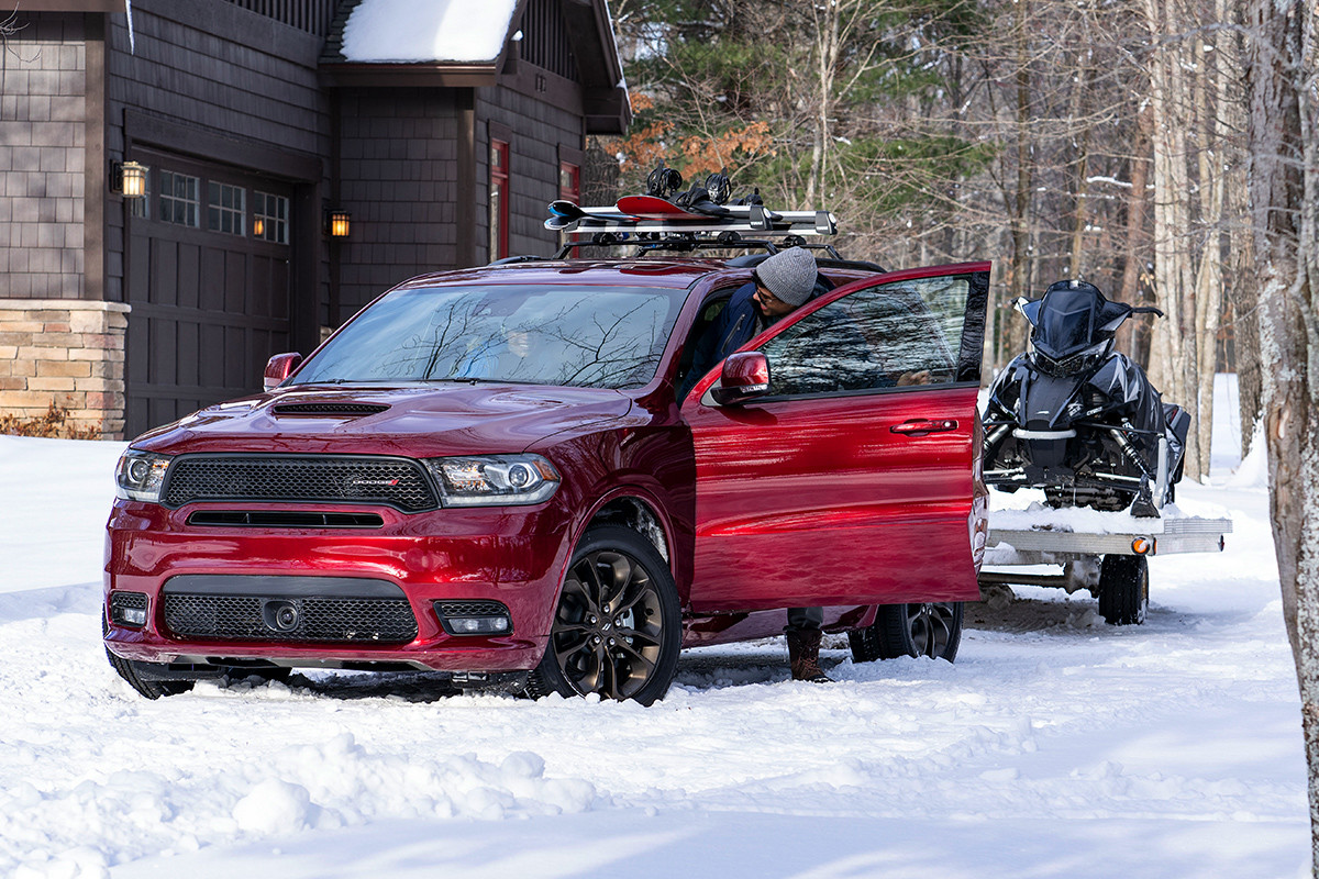 Front view of the red 2019 Dodge Durango parked in the snow outside of a mountain cabin, towing a snowmobile