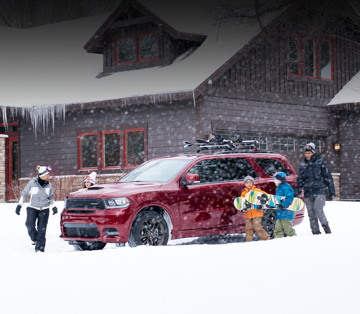 Red 2019 Dodge Durango parked in the snow in front of a mountain cabin, surrounded by a family