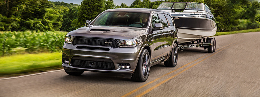 Un Dodge Durango 2019 gris remorquant un bateau noir et blanc sur une route de campagne.