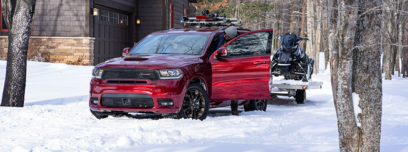 Front view of the red 2019 Dodge Durango parked in the snow outside of a mountain cabin, towing a snowmobile