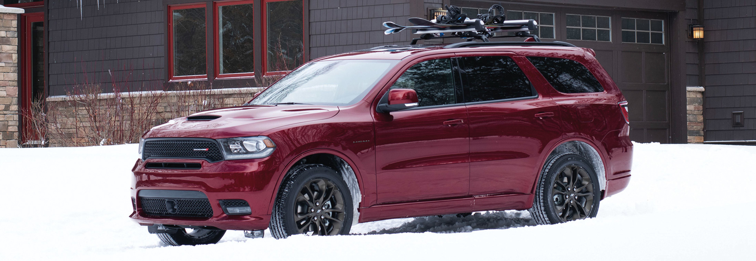 Dodge Durango 2020 rouge stationné devant la maison en hiver avec des planches à neige sur le porte-bagages de toit.