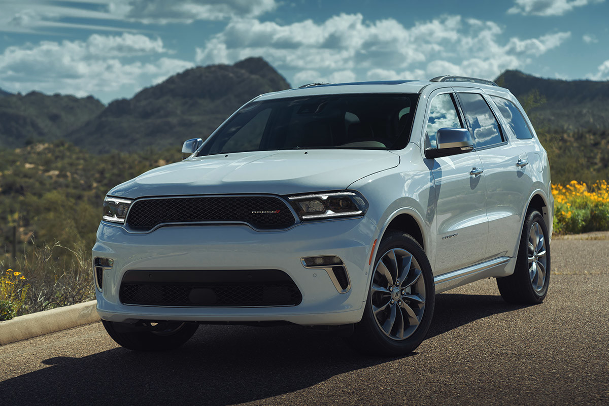 Dodge Durango blanc garé à côté d’un trottoir avec des montagnes, des fleurs sauvages et un ciel bleu en arrière-plan.