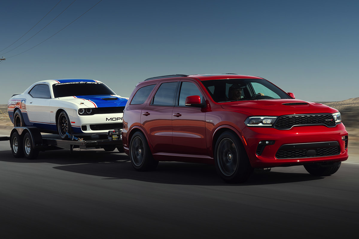 Red Dodge Durango towing a trailer with a SRT® Hellcat affixed to it.