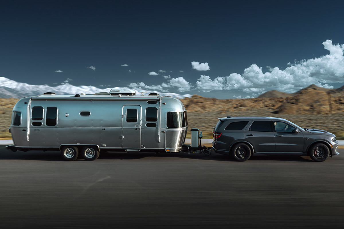 Vue latérale d’un Dodge Durango gris descendant une route tout en tirant une remorque, avec des collines et un ciel bleu en arrière-plan.