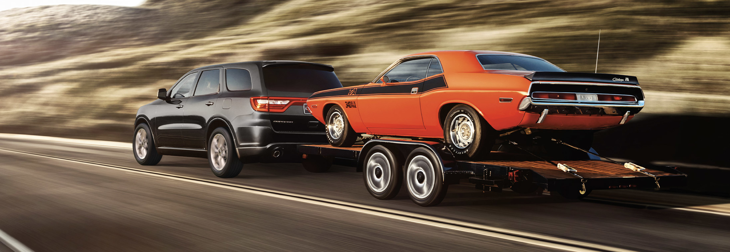 A red 2022 Dodge Durango towing a car on a trailer behind it