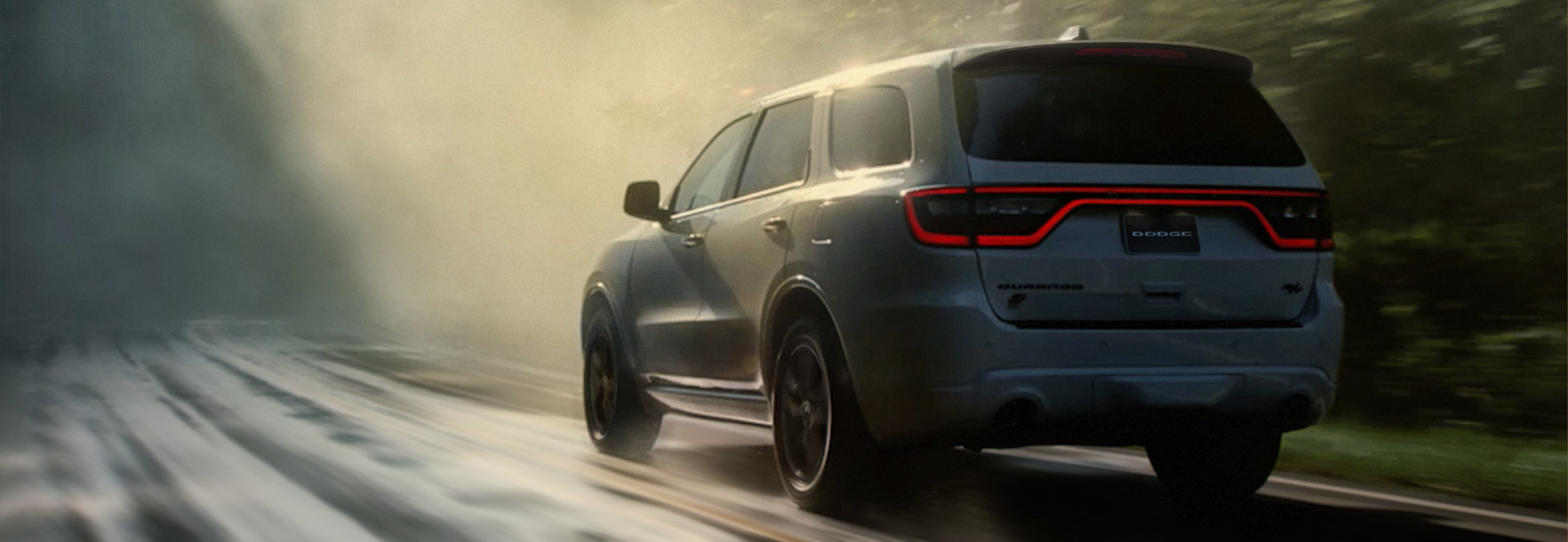 L’extérieur arrière d’un Dodge Durango 2022 blanc roulant sur une route de campagne poussiéreuse