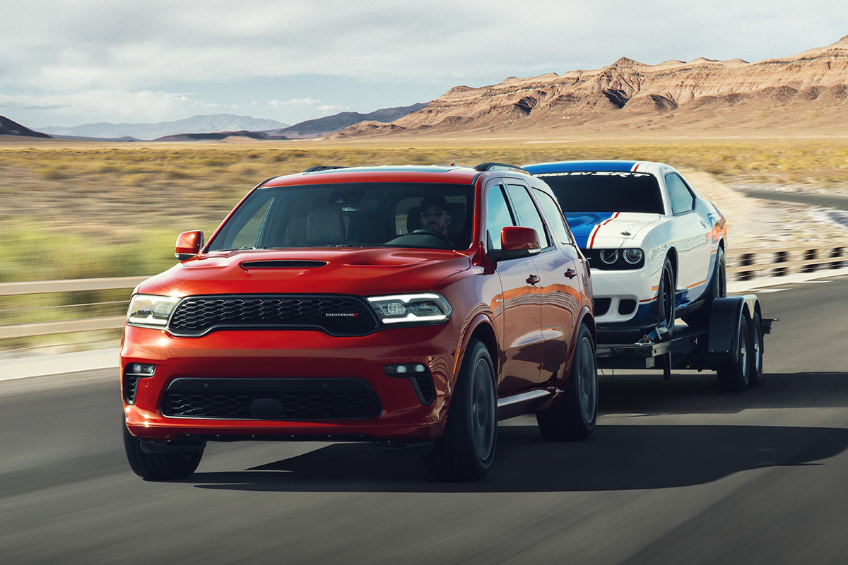 A red 2022 Dodge Durango towing a white car with a blue stripe ontop of a trailer