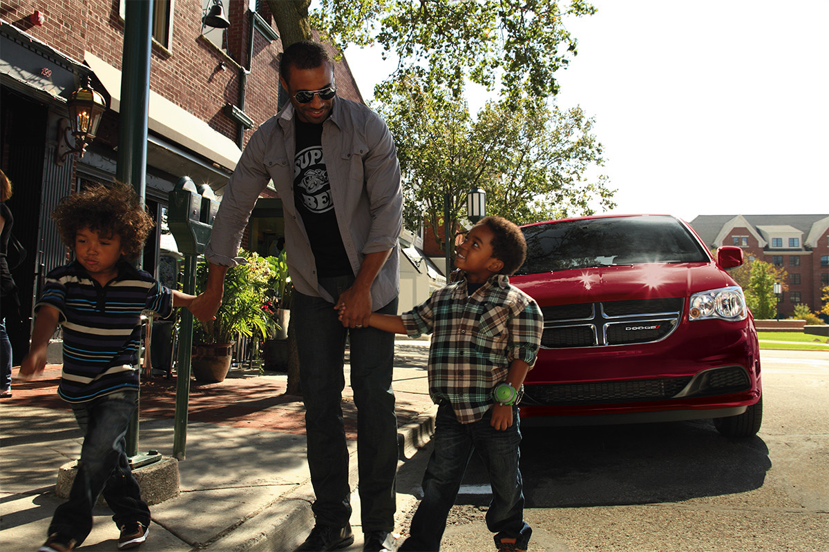 A red 2020 Dodge Grand Caravan parked on a street while two children and a man walk in front of it