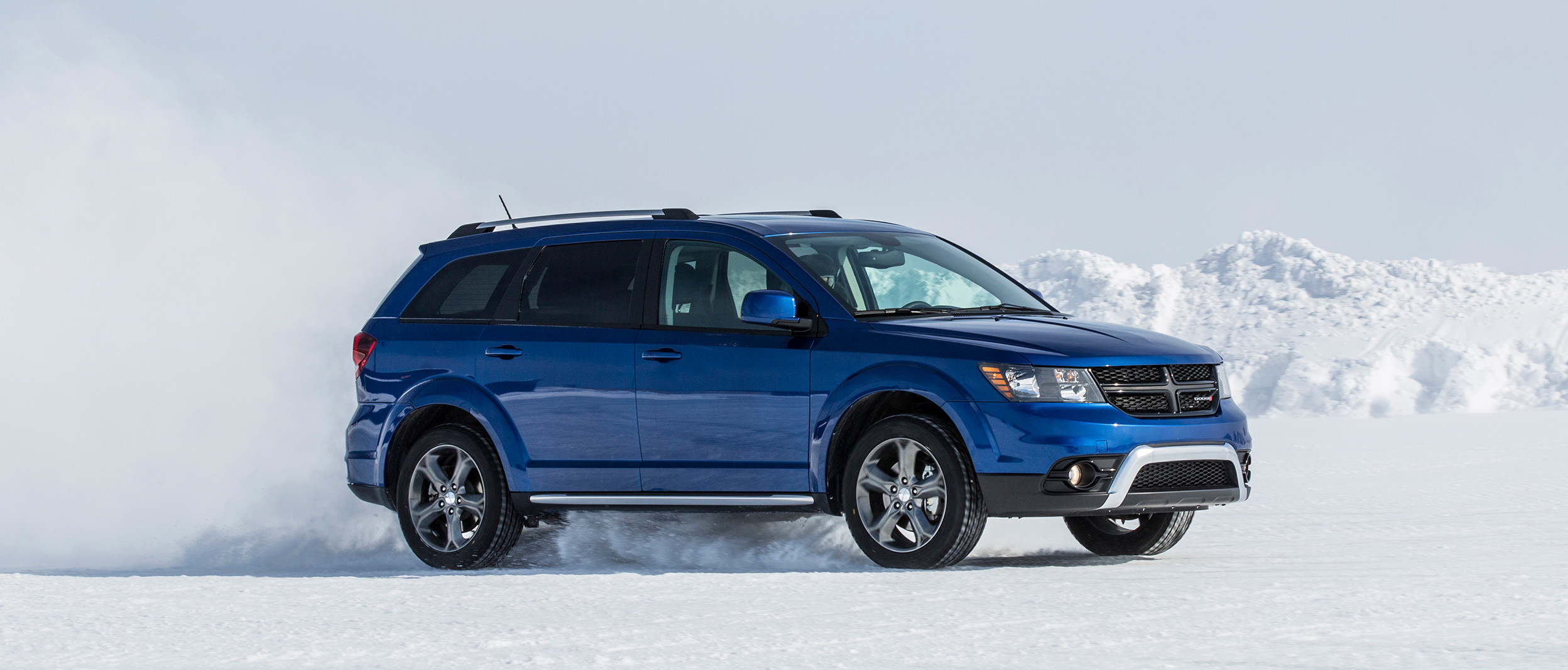 Vue latérale du Dodge Journey 2019, illustré en bleu, roulant à travers un champ enneigé dans les montagnes