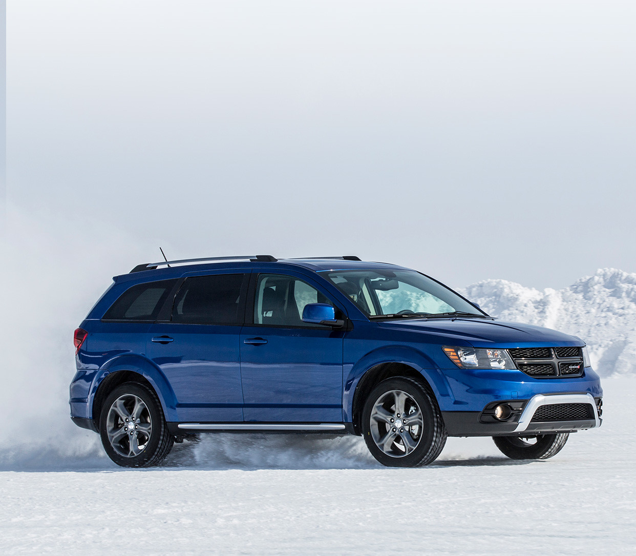 Vue latérale du Dodge Journey 2019, illustré en bleu, roulant à travers un champ enneigé dans les montagnes