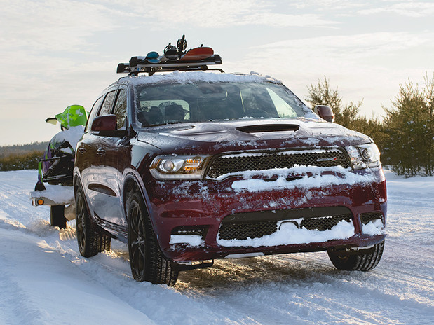 Vue de face du Dodge Durango 2020, illustré en rouge, stationné sur une route enneigée près d’un couple qui marche