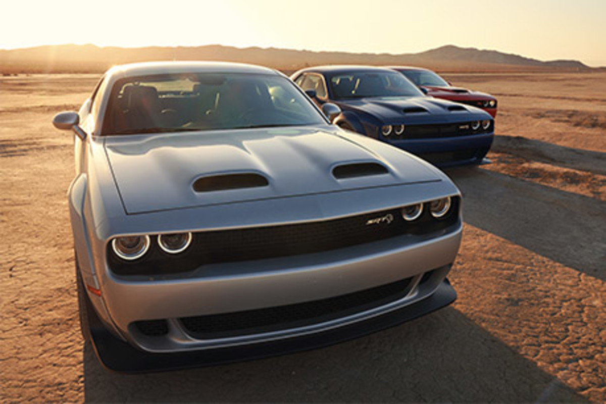 Trois Dodge Challenger, toutes garées dans un désert avec une montagne en arrière-plan.