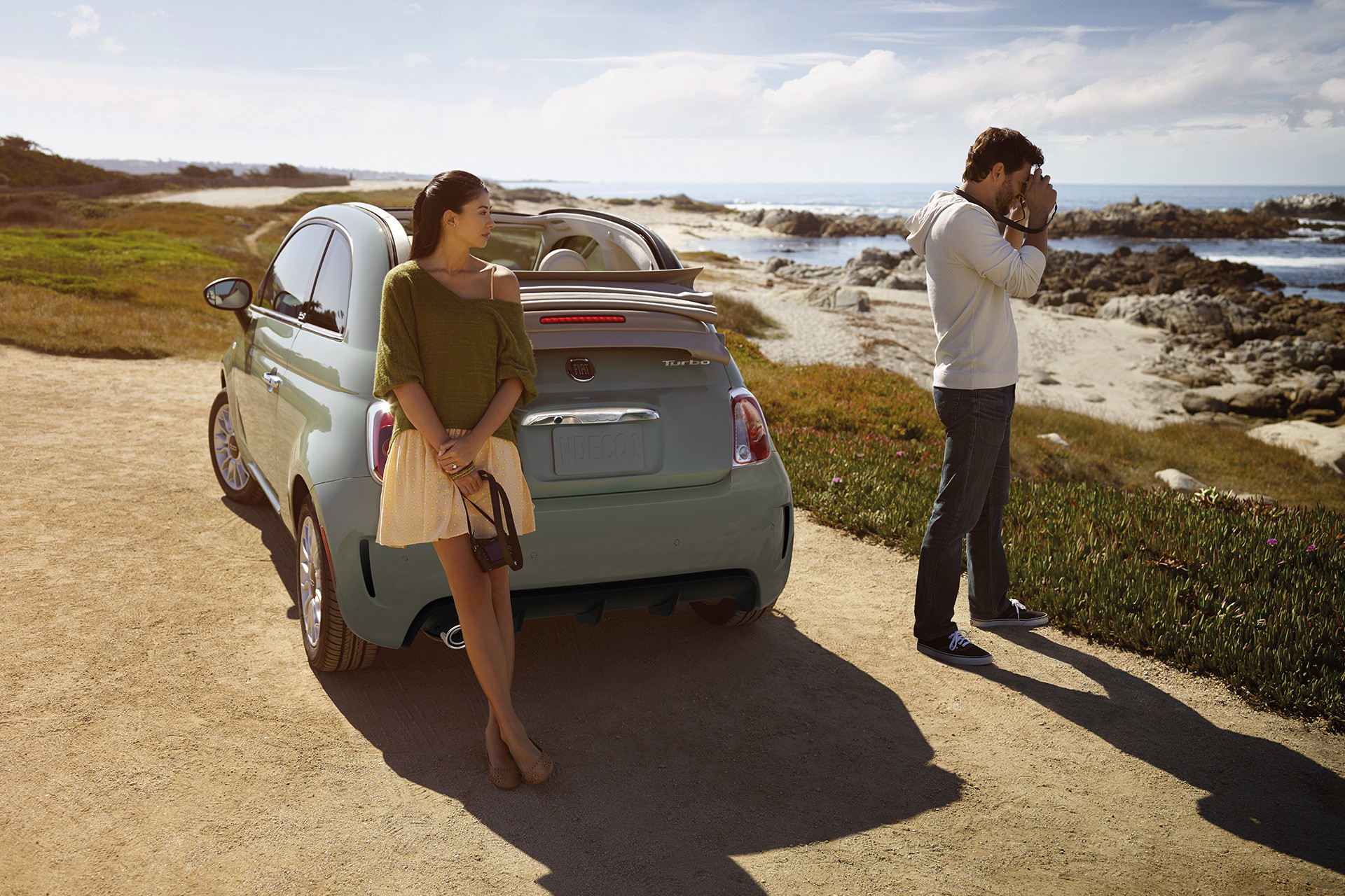 Fiat 500 Lounge 2018 grise stationnée au sommet d’une colline avec une femme s’appuyant contre la voiture.
