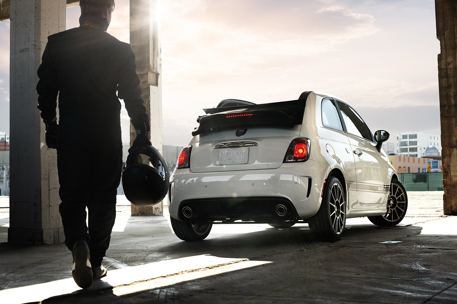 Pilote de course professionnel marchant vers une Abarth Cabrio blanche stationnée avec sa capote baissée.
