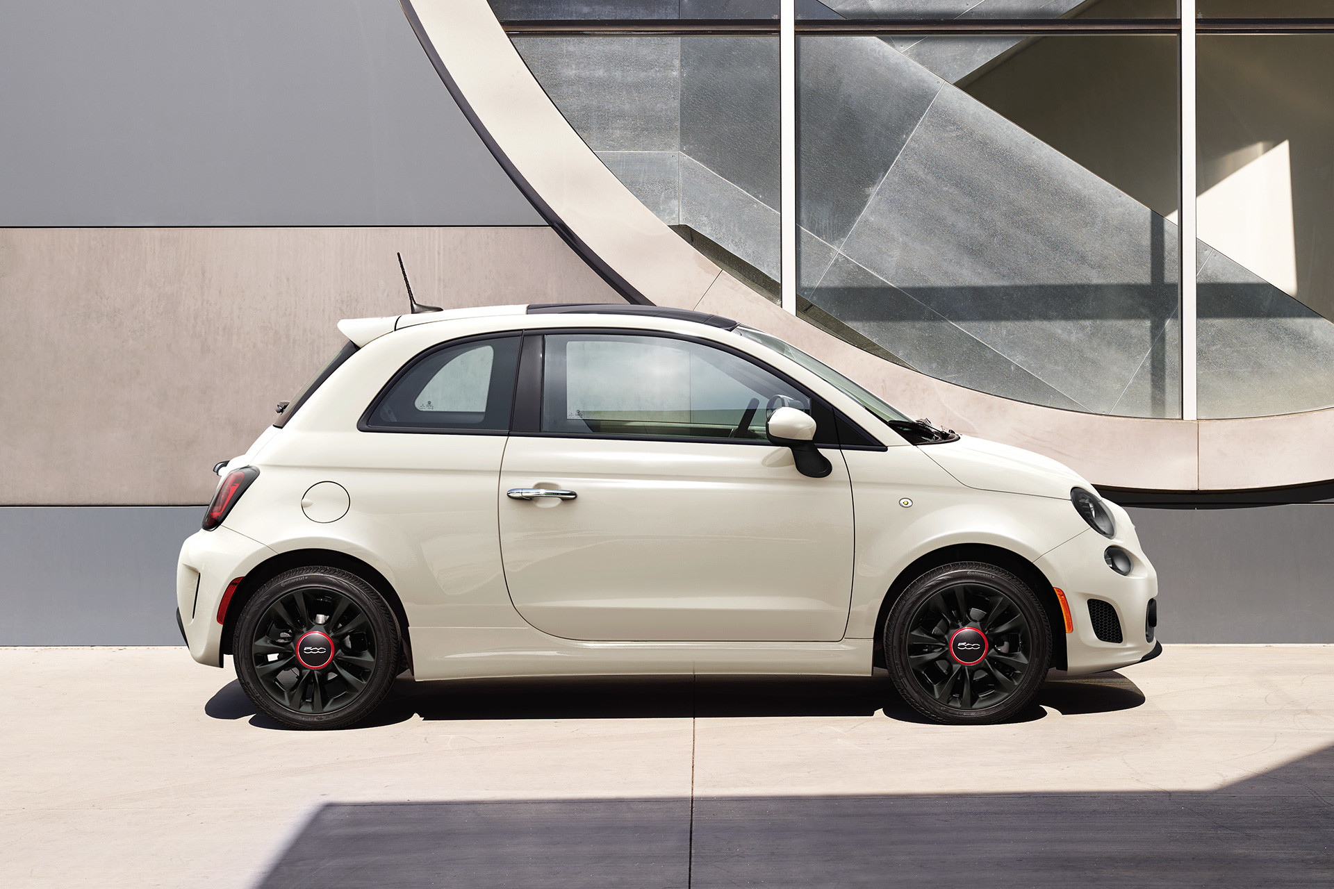 Une FIATMD 500 Cabrio blanche stationnée devant un édifice moderne.