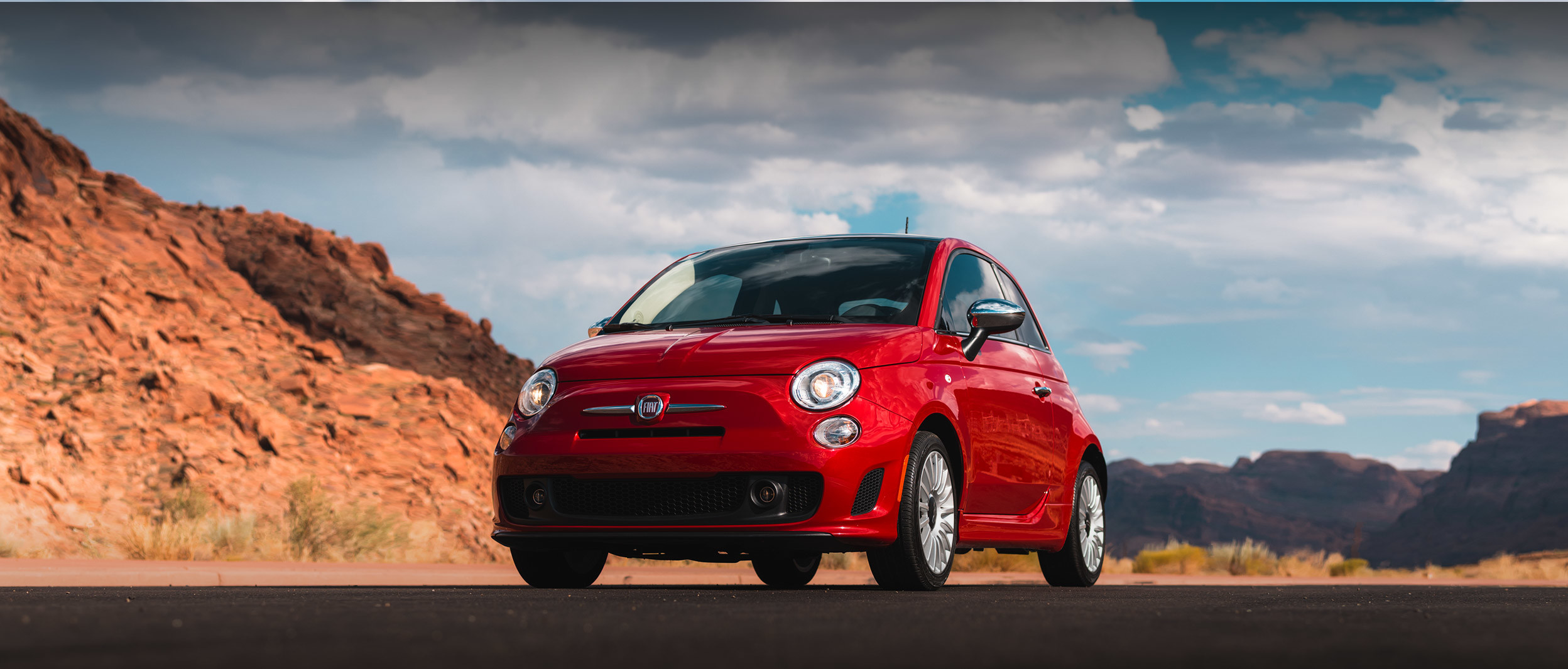 Red 2019 FIAT® 500 parked on a road outdoors by mountains.