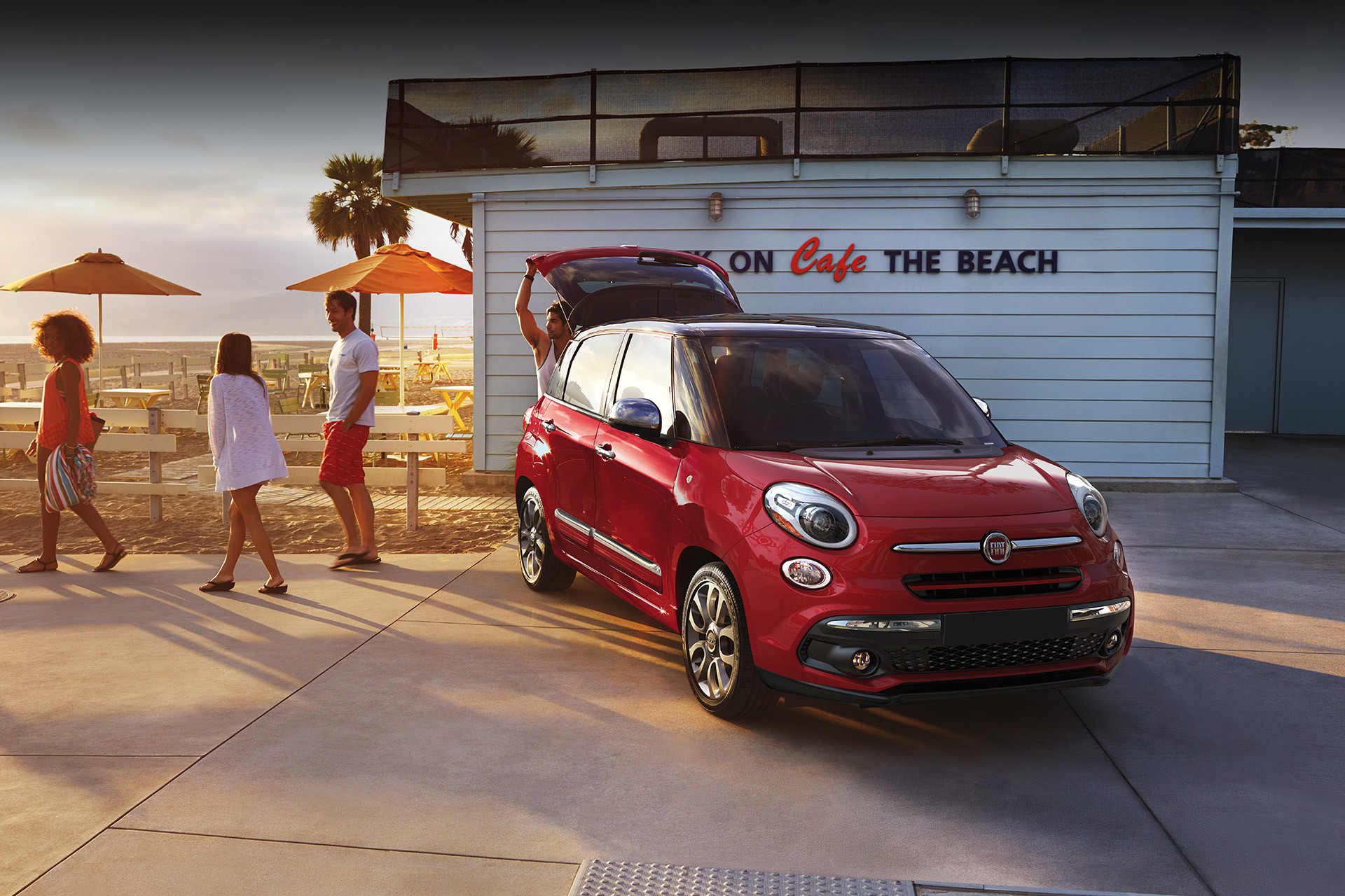 Vue de la FIAT 500L 2019 garée sur la promenade d’une plage avec le coffre ouvert, illustrée en rouge