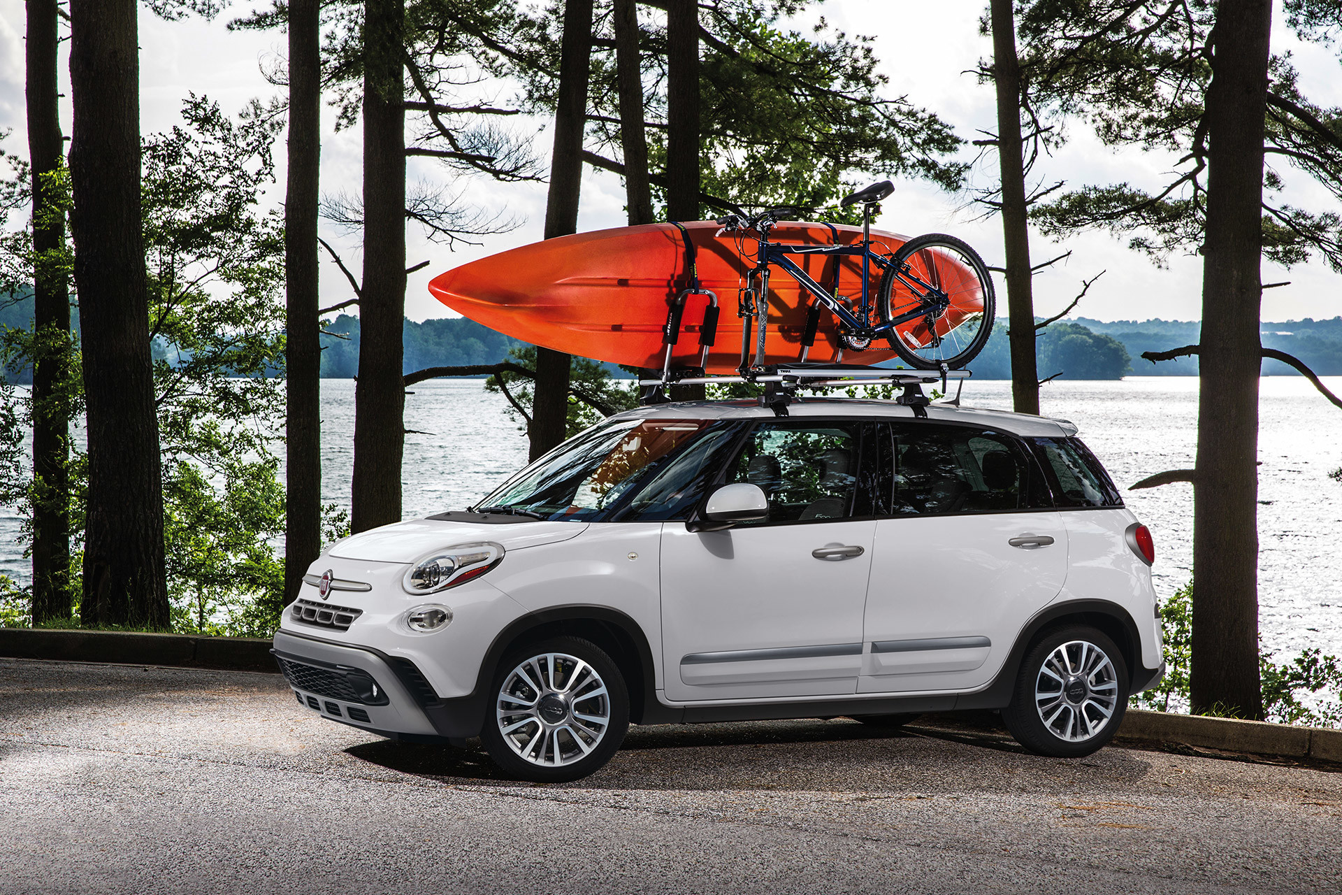 FIAT 500L 2019 garée près d’un lac avec un vélo et un kayak sur le toit, illustrée en blanc
