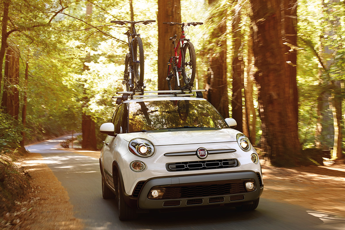 The 2020 Fiat 500L being driven on a road in a forest with two bicycles on the roof through trees