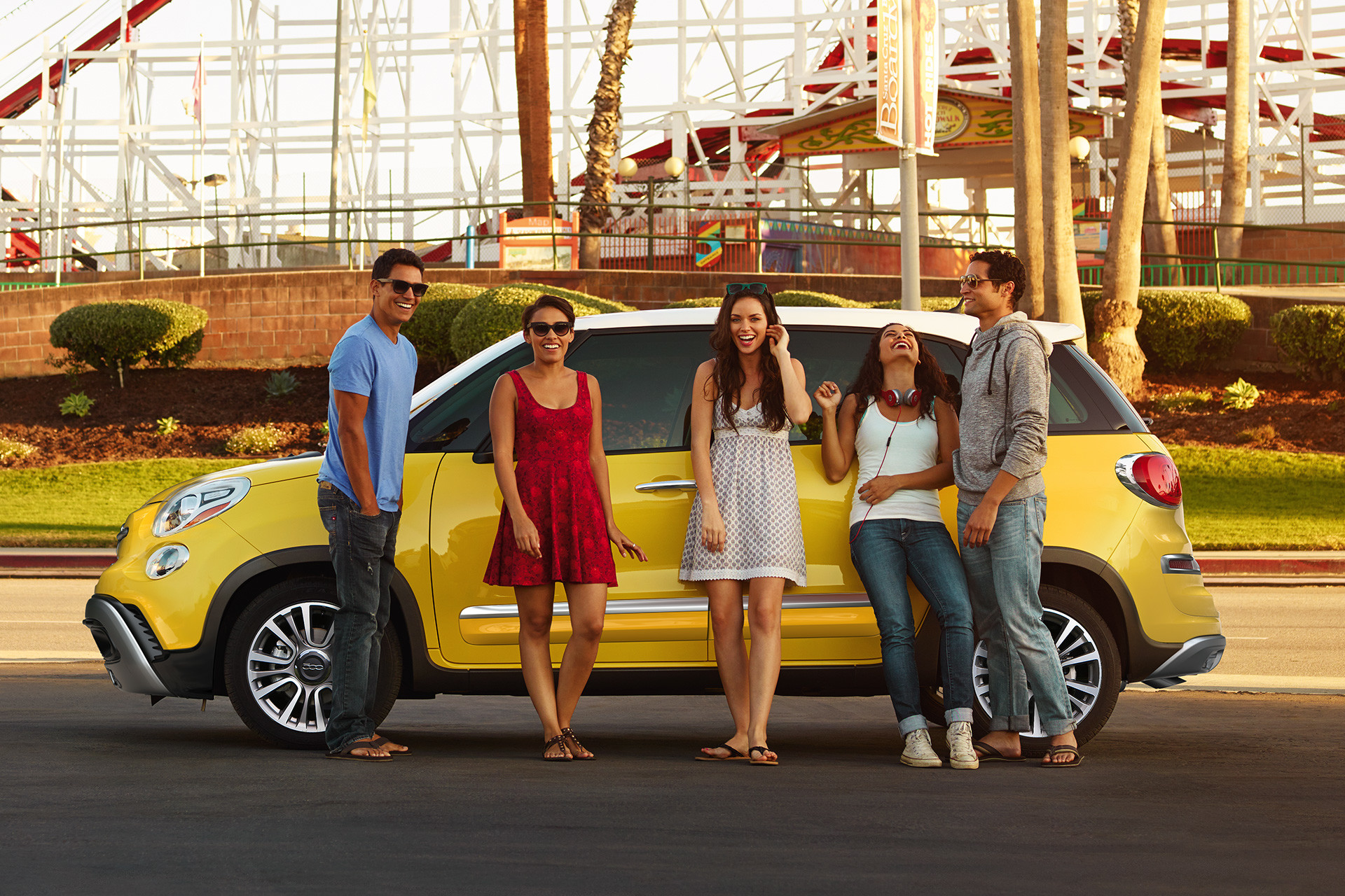 People standing next to the 2020 Fiat 500L parked in a parking lot in front of roller coaster