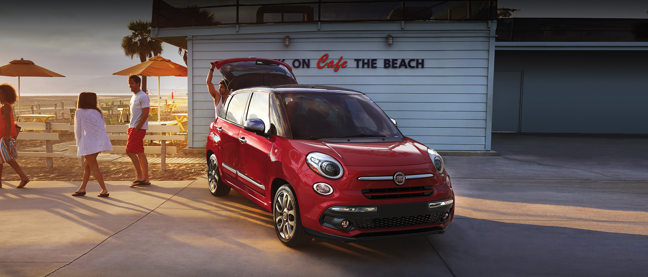 The 2020 Fiat 500L parked on a driveway beside two people during the sunset