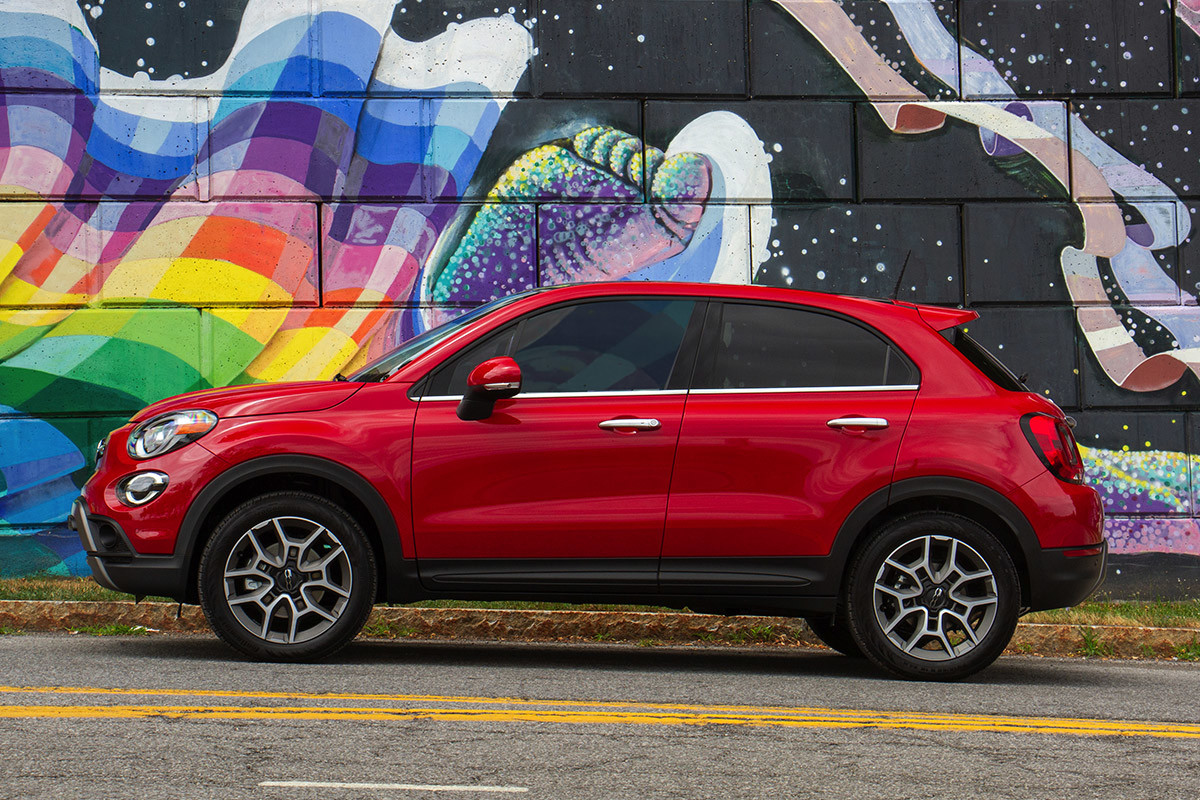 Une FIAT 500X 2020 rouge garée sur une route à côté d’un mur coloré