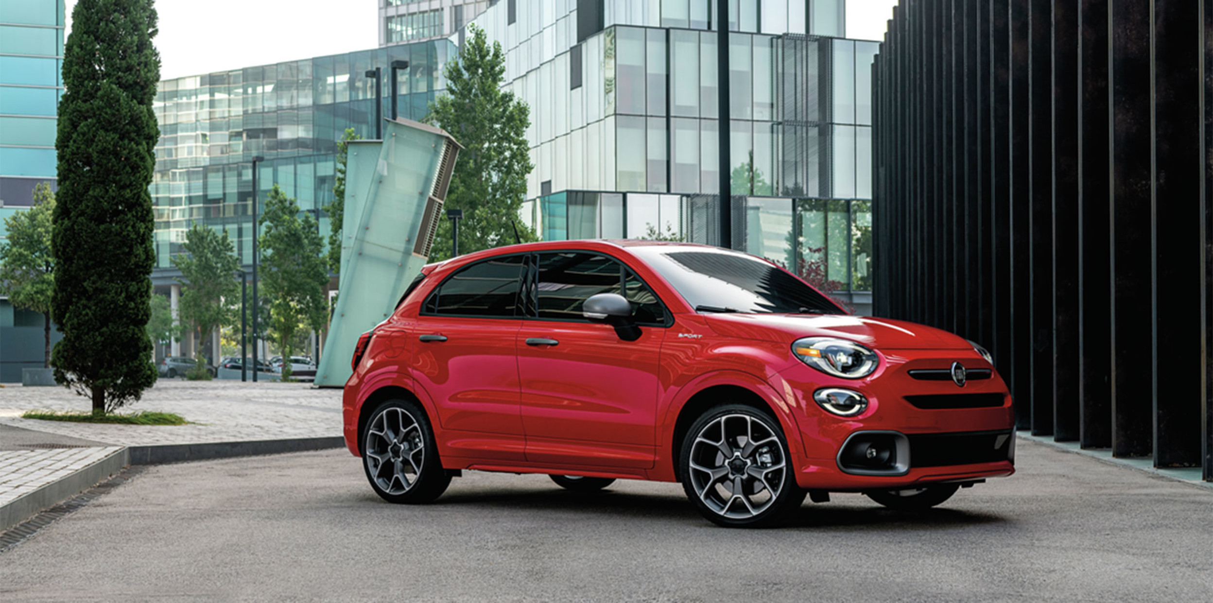Red Fiat 500X parked in front of a glass building.