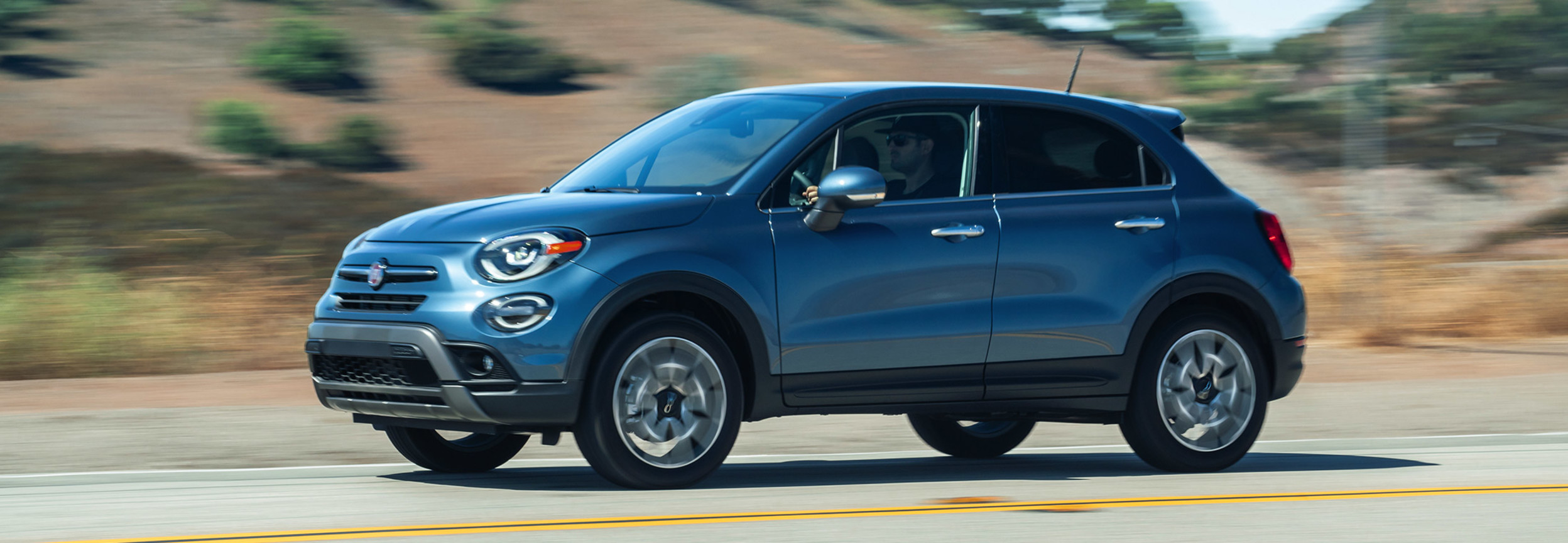 Side view of a blue 2021 FIAT 500X driving on a road with a desert in the background