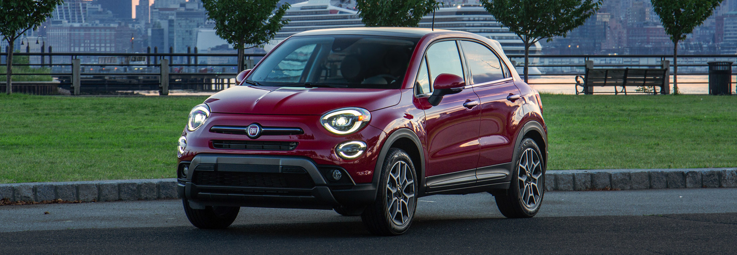 Side view of a red FIAT 500X parked in a lot with a cruise ship in the background