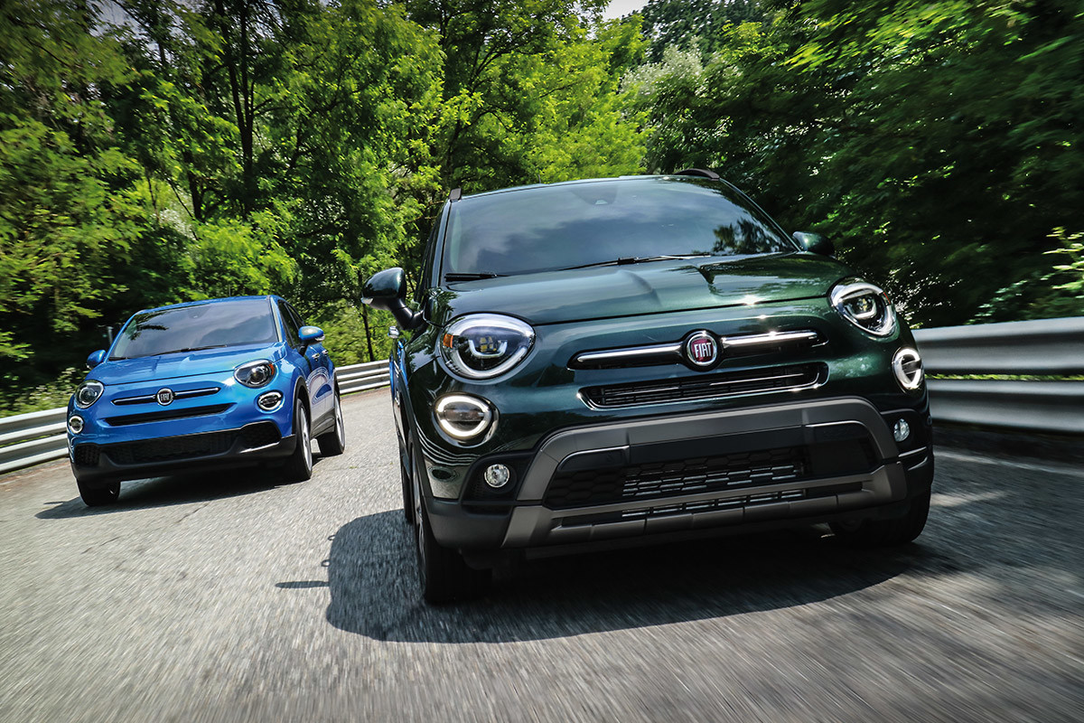Front view of a blue 2021 FIAT 500X and a green 2021 FIAT 500X driving on a road with trees in the background