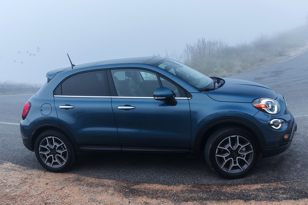 Side view of a blue FIAT 500X parked on the side of the road in foggy conditions