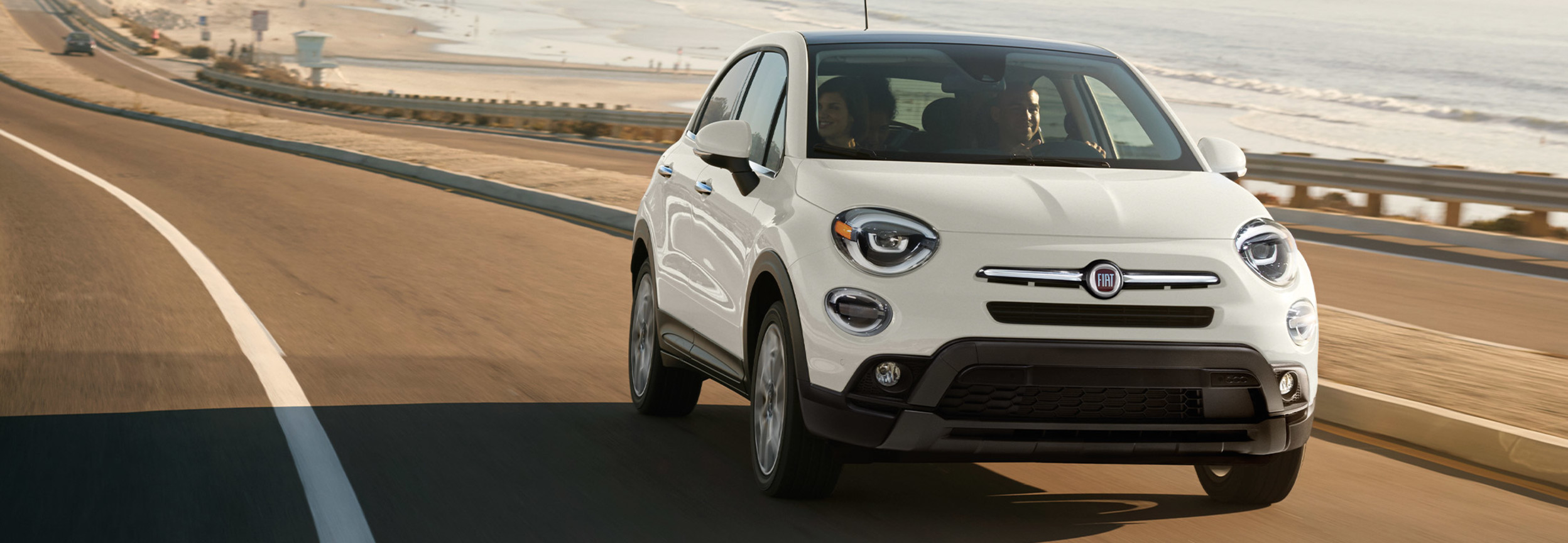 A white 2022 FIAT 500X driving down a highway by the ocean.