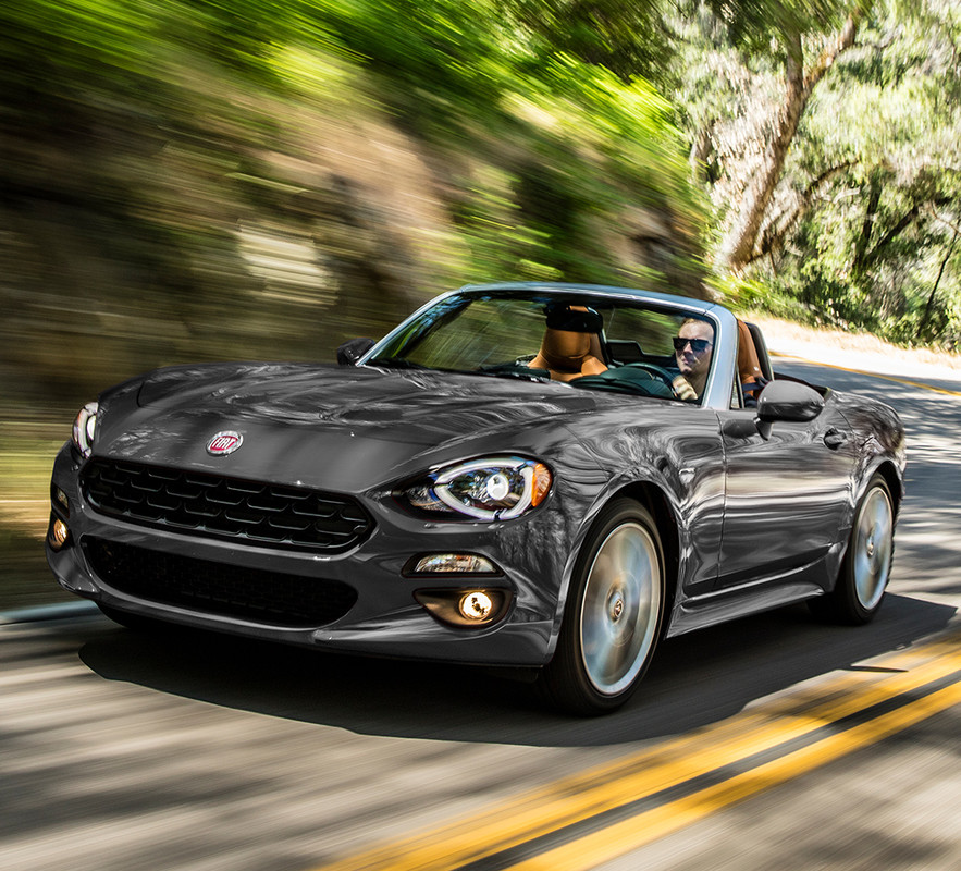 Two people riding a Grey 2019 FIAT 124 Spider along a curved road