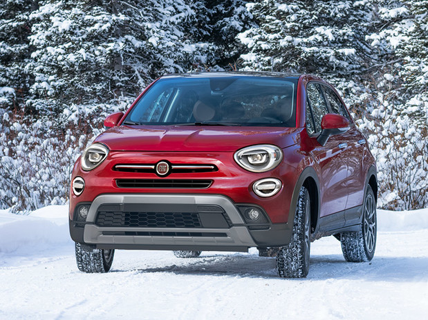 Fiat 500X bourgogne roulant sur un sentier enneigé entouré de grands arbres couverts de neige.