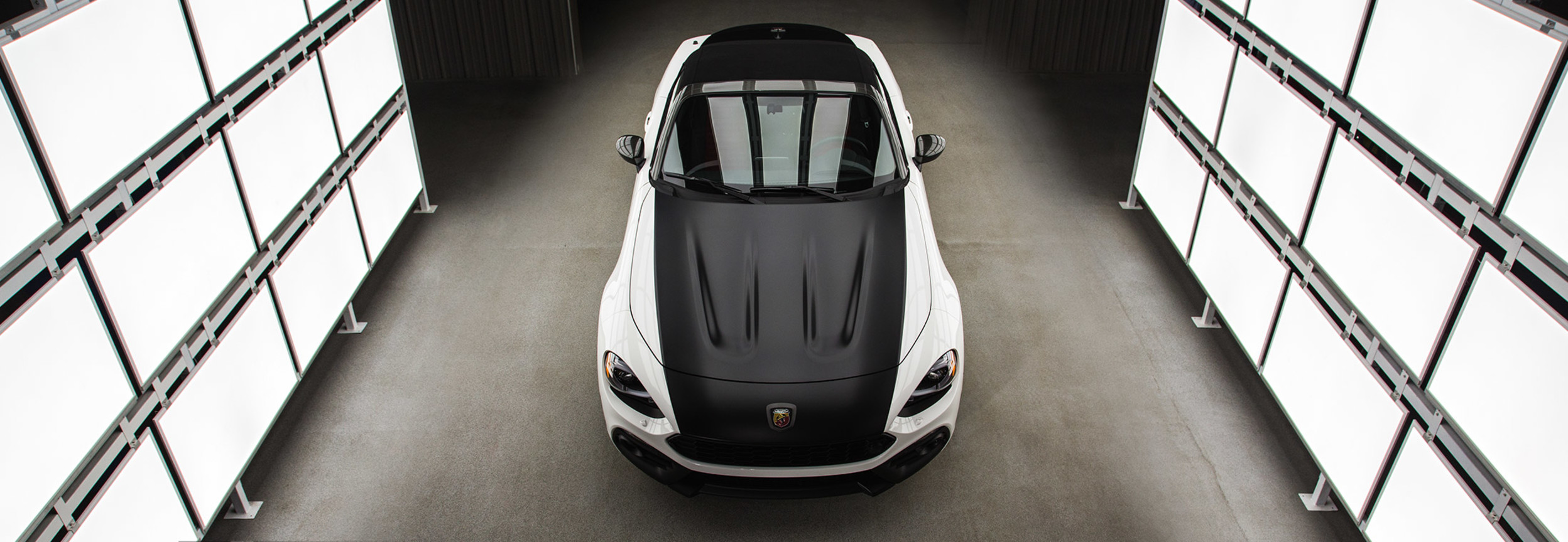Birds eye view of Black & White 2020 FIAT 124 Spider parked in an enclosed garage surrounded by illuminating lights