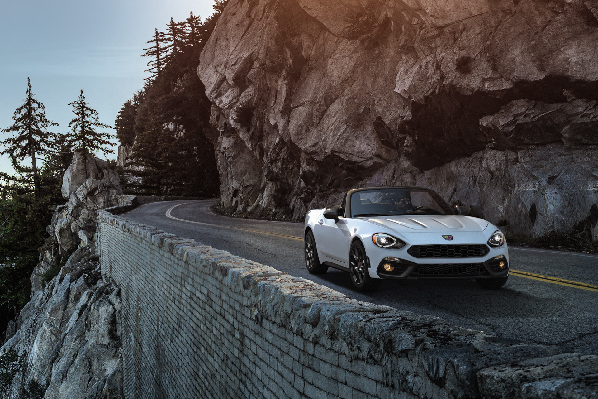 The 2020 FIAT 124 Spider driving on a road beside cliffs through mountain