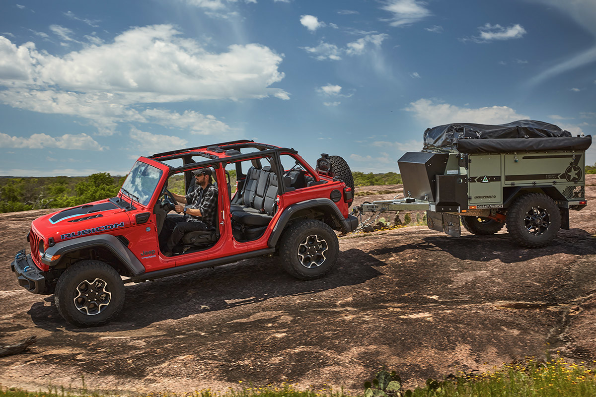 The side of a red 2022 Jeep Wrangler 4xe towing a mini camper.