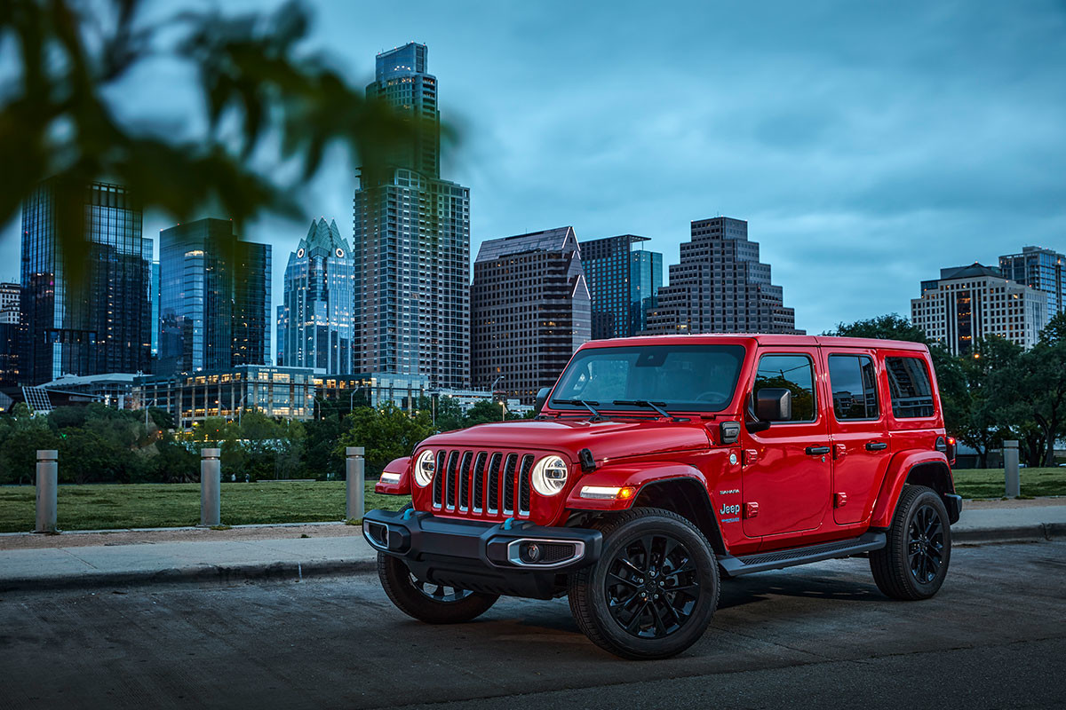 Une Jeep Wrangler 4xe rouge 2022 avec ses phares à LED allumés, garée dans la rue avec des gratte-ciel en arrière-plan.