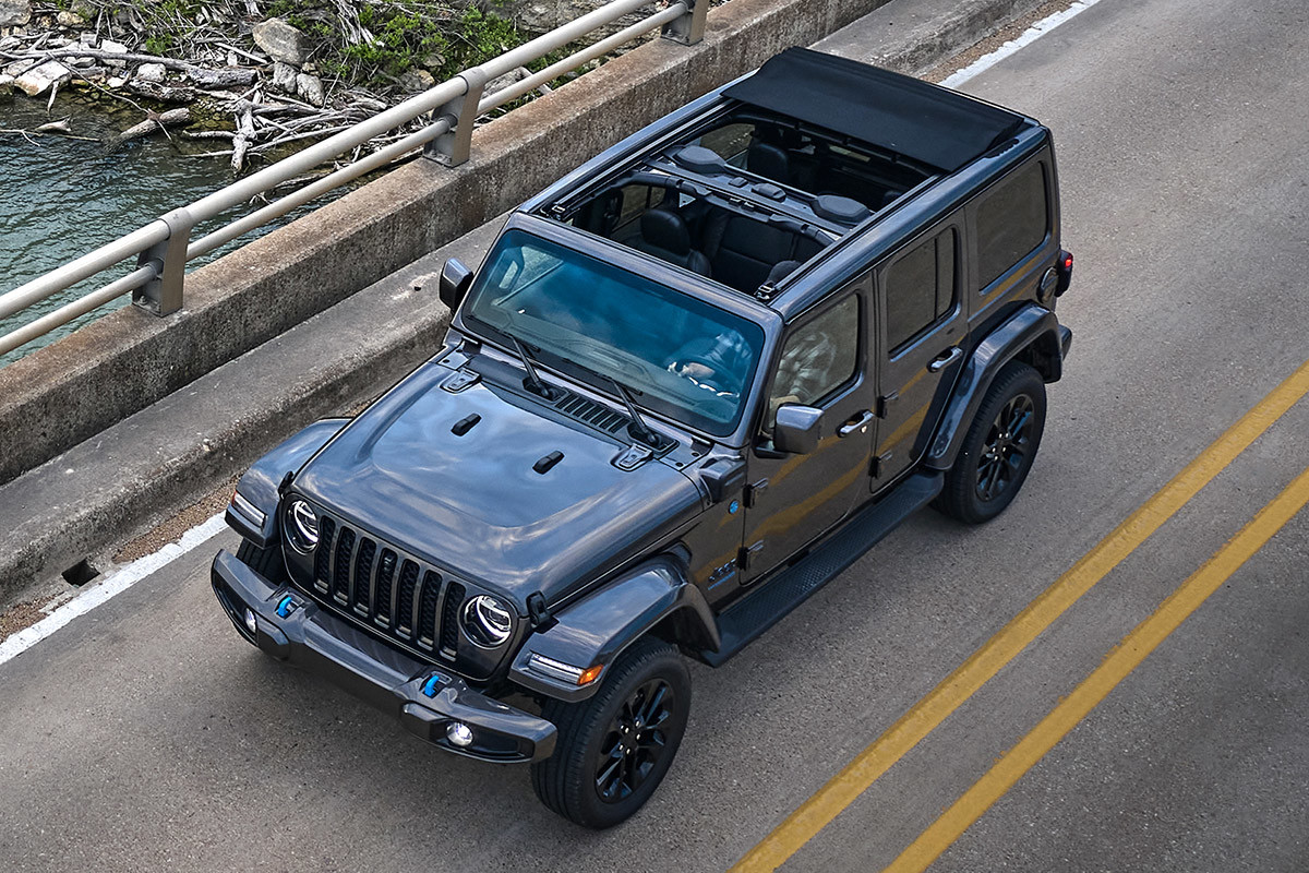 Vue de haut en bas d’un Jeep Wrangler 4xe 2022 gris roulant sur un pont au-dessus de l’eau avec le toit baissé.