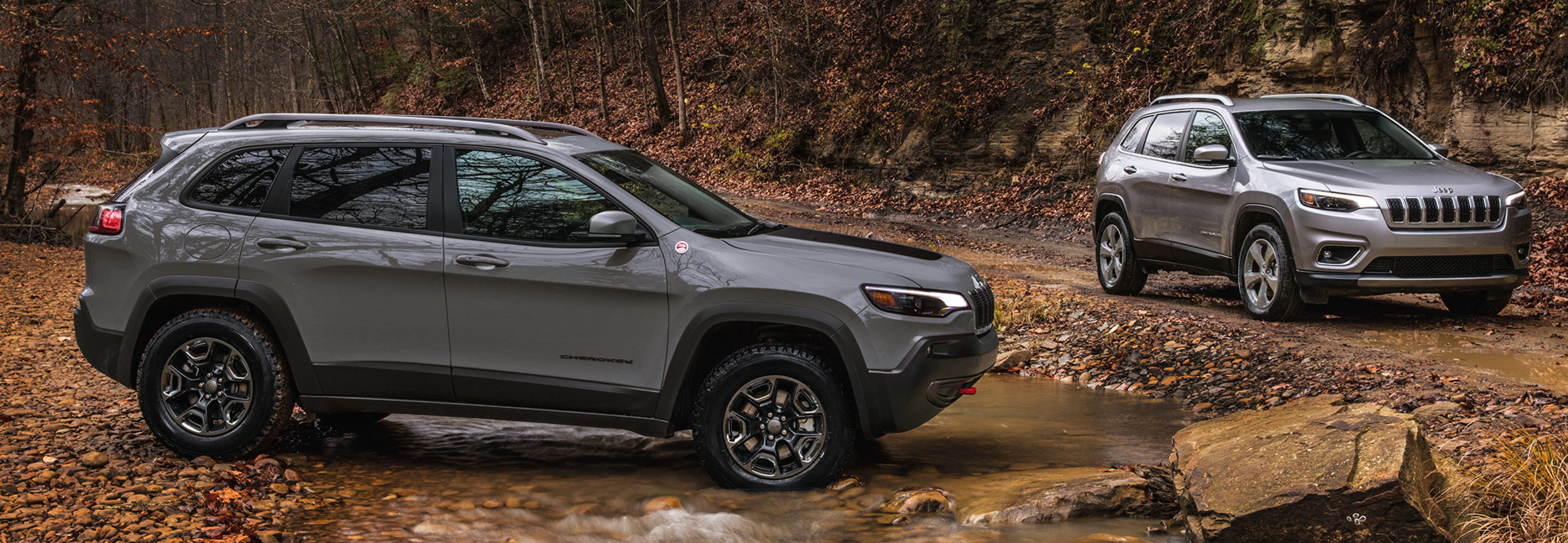Two silver Jeep Cherokees near a stream of water