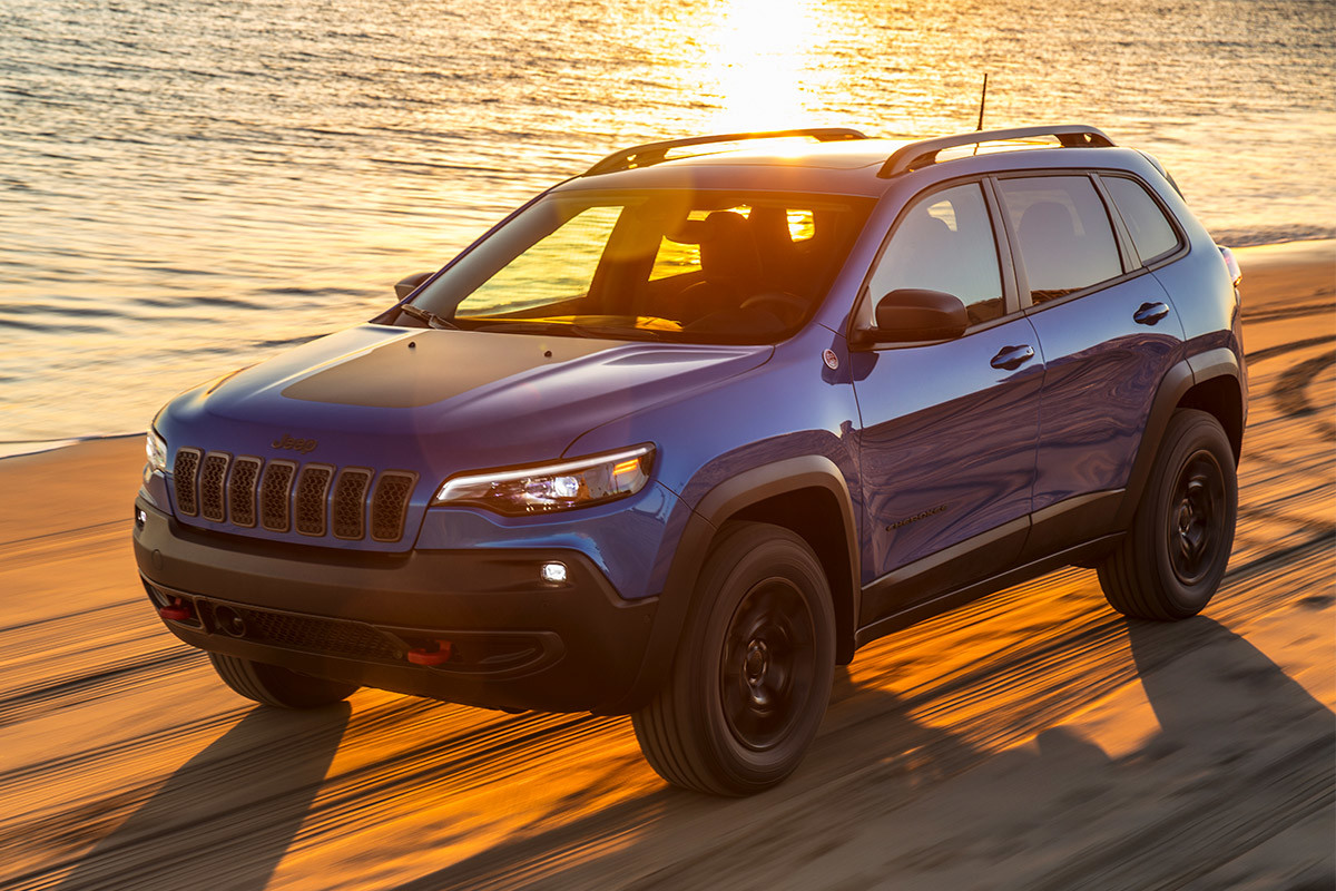 Front of quarter view of blue 2020 Jeep Cherokee being driven on beach sand in the sunset
