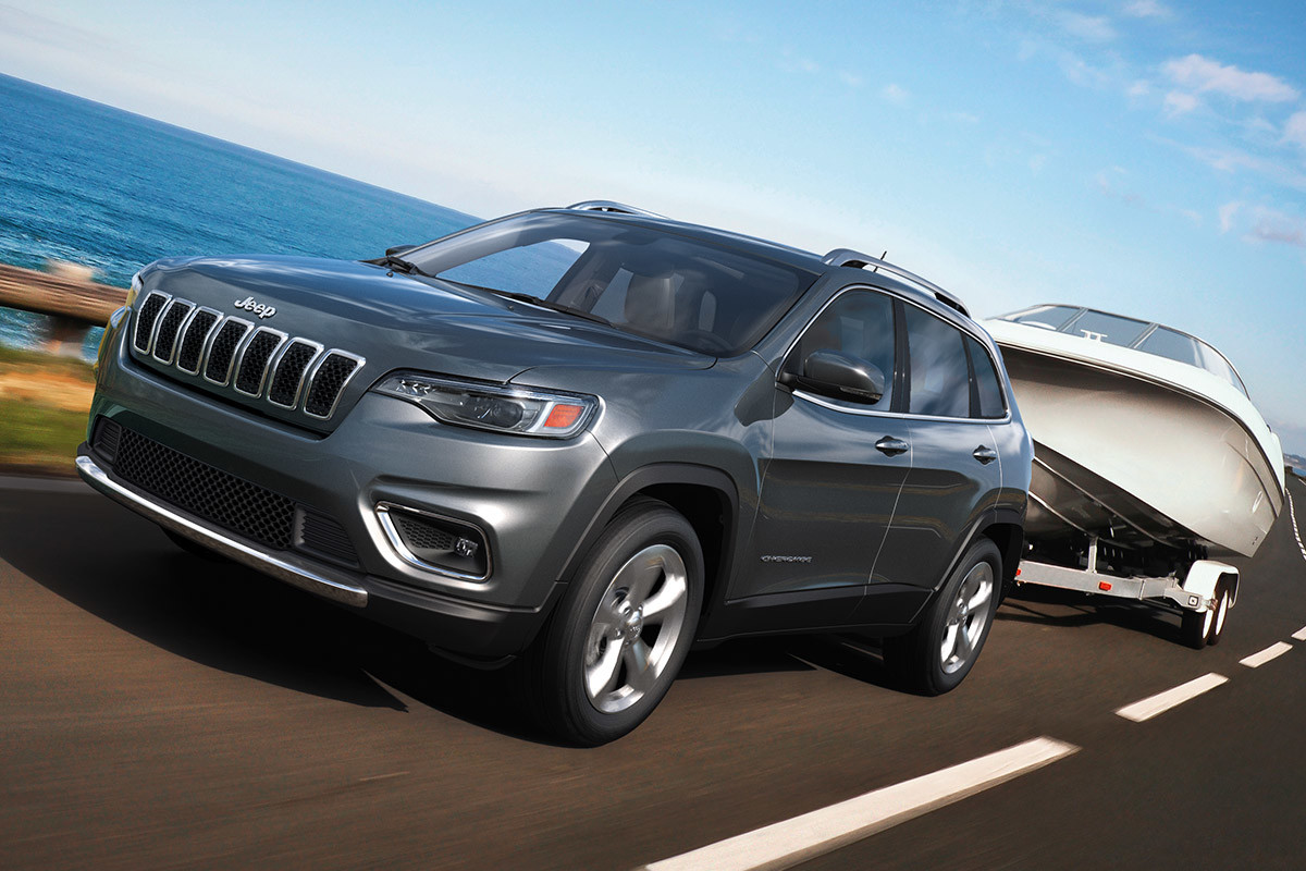 Jeep Cherokee 2021 remorquant un bateau le long d’une autoroute donnant sur la rive.