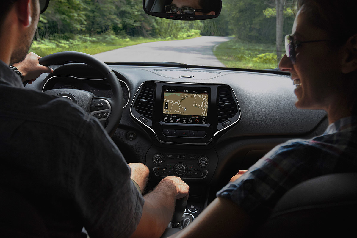 View from the rear seat of a 2021 Jeep Cherokee showing a happy couple enjoying a drive on a country road.