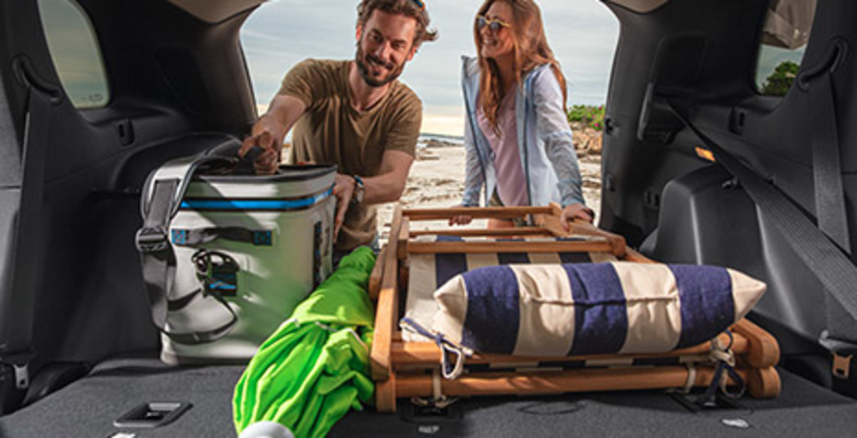 EXPERTLY DESIGNED A view of a man and a woman unloading a beach chair, an umbrella, and a picnic basket from the cargo area of a 2021 Cherokee.